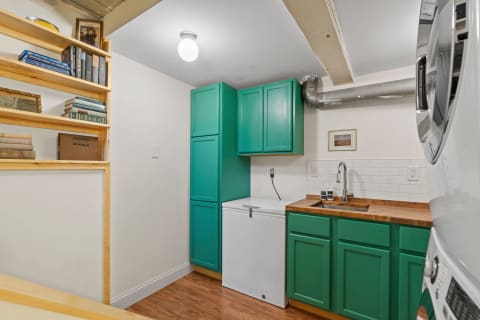 A cozy laundry area with turquoise cabinets and a wooden countertop, featuring a sink and a white freezer underneath.