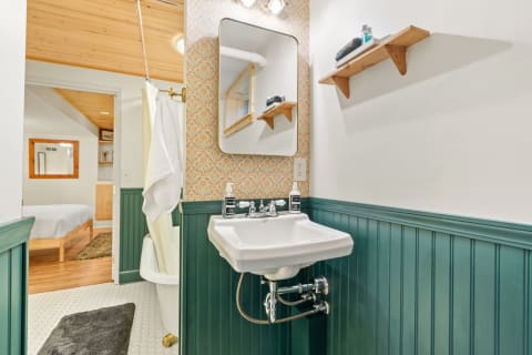 Charming bathroom with green wainscoting, patterned wallpaper, and a vintage-style sink.