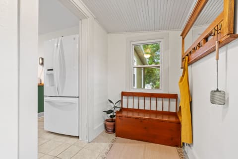 Bright entryway leading to a kitchen with a white refrigerator, wooden bench, and yellow apron.