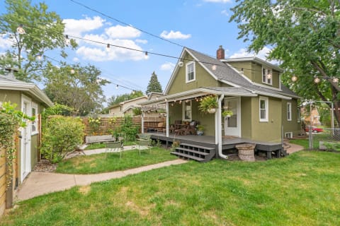 A green house with a deck and backyard seating, adorned with string lights and potted plants.