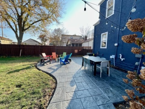A backyard patio featuring colorful Adirondack chairs and a blue house.