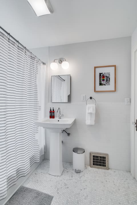 A modern bathroom with a white pedestal sink, striped shower curtain, and hexagon tile floor.