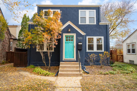 A blue two-story house with a turquoise front door in an autumn setting.