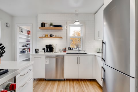 Modern kitchen with white cabinets, stainless steel appliances, and a window overlooking autumn trees.