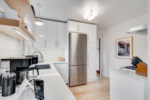 A modern kitchen featuring white cabinets, a stainless steel refrigerator, and a coffee maker.