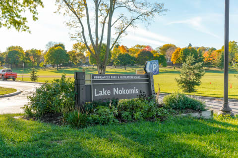 Welcome sign for Lake Nokomis surrounded by greenery and autumn trees.