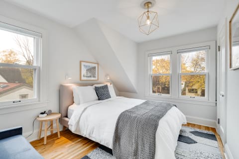 A contemporary bedroom featuring a slanted ceiling, bright white bedding, and autumn view through the windows.