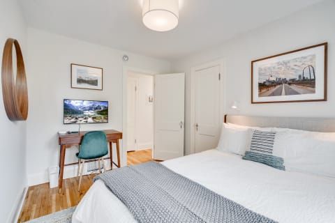 Cozy bedroom featuring a bed, desk with TV, and framed artwork.