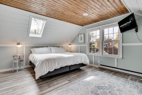 Cozy bedroom with white linens, wooden ceiling, and natural lighting from a skylight.