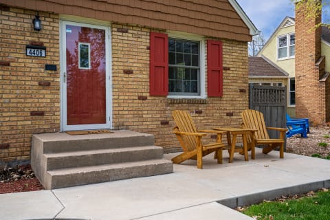 A house exterior featuring a red door, red shutters, and wooden chairs on the porch.