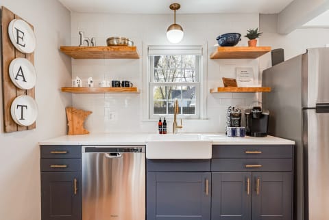 A modern kitchen corner with wooden shelves, dark cabinets, and a farmhouse sink.