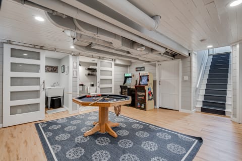 Modern basement rec room with game table and arcade machines.