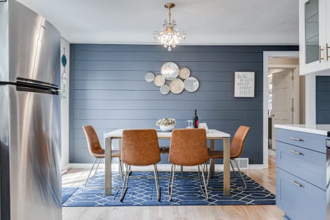 A contemporary dining space with a blue accent wall, a white table, and brown chairs.
