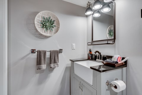Modern bathroom with a white sink, dark countertop, and gray towels hanging.