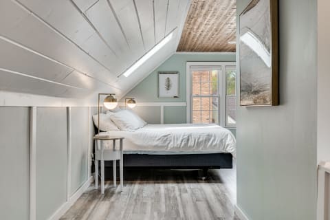 A cozy attic bedroom featuring a bed, wall-mounted lamps, and wooden ceilings.