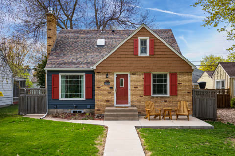 Charming house with brick and wooden elements, red shutters, and a patio area with Adirondack chairs.