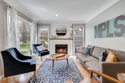 Modern living room with a gray sofa, blue chairs, and a fireplace, adorned with decorative elements and natural light.