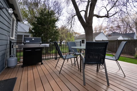 Outdoor deck with a grill and seating area surrounded by trees and fence.