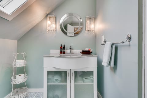 A stylish attic bathroom featuring a white vanity, crystal sconces, and a pale blue color scheme.