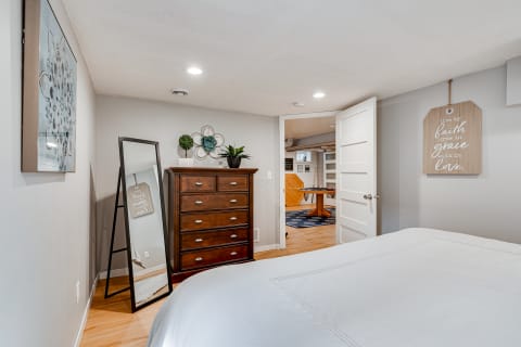 Cozy bedroom with a white bed, wooden dresser, mirror, and inspirational wall decor.