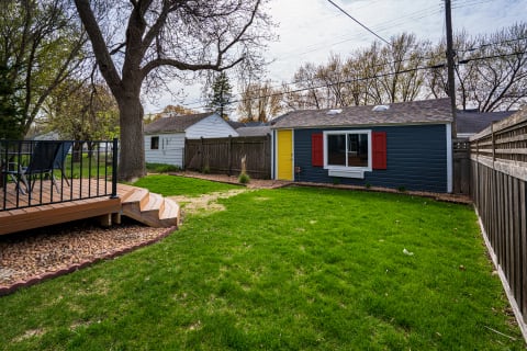A backyard featuring a blue shed, wooden deck, and lush green lawn.