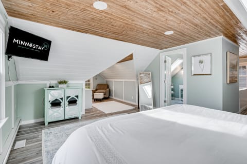 A well-decorated attic bedroom featuring a sloped ceiling, light mint walls, and a comfortable bed.