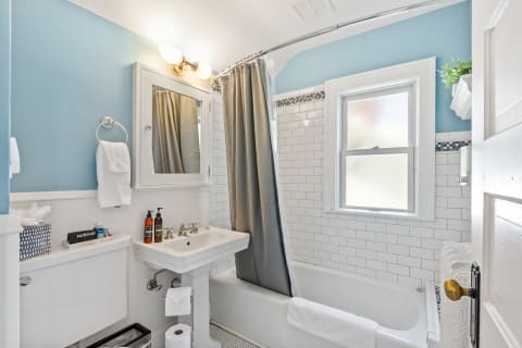 A clean bathroom with a bathtub, pedestal sink, and soft blue walls.