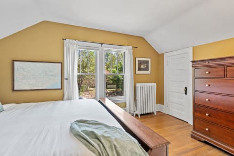 Cozy bedroom with yellow walls, wooden furniture, and large windows.
