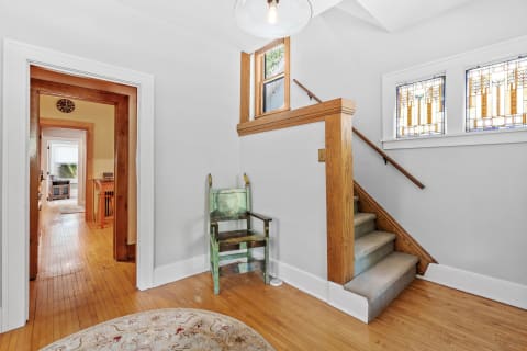 A hallway entrance featuring a unique green chair, stained glass windows, and a staircase.
