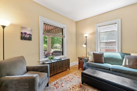A warmly decorated living room featuring a blue sofa, a grey armchair, and a view of the outdoors.