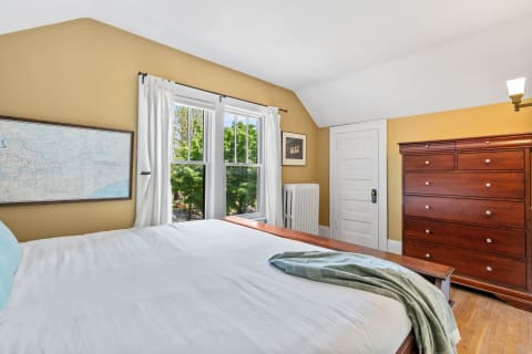 Cozy bedroom featuring a bed, large windows with curtains, a vintage map on the wall, and a wooden dresser.
