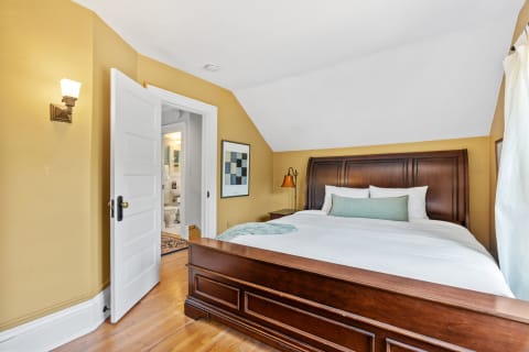 Cozy bedroom featuring a wooden bed, golden yellow walls, and a modern art piece.