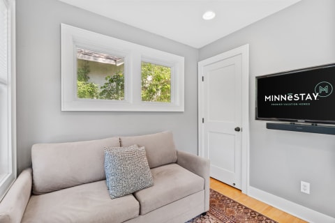 Cozy room with a beige couch, large windows, and a TV displaying the Minnestay logo.
