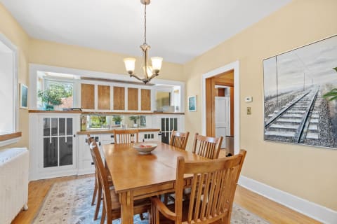 Cozy dining room with wooden table, chairs, and a bowl of fruit, featuring pale yellow walls and a window view.