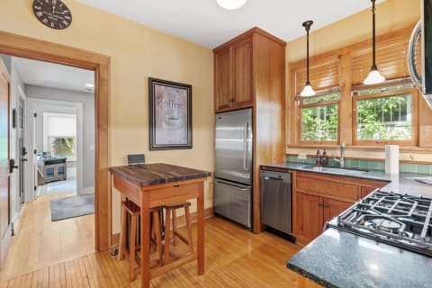 A cozy kitchen with wooden furniture, stainless steel appliances, and large windows.
