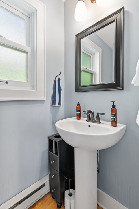 A small bathroom featuring a white pedestal sink, modern decor, and soft blue walls.