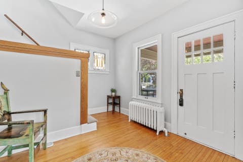 A cozy entrance hall with gray walls, a wooden divider, a green chair, and stained glass windows.