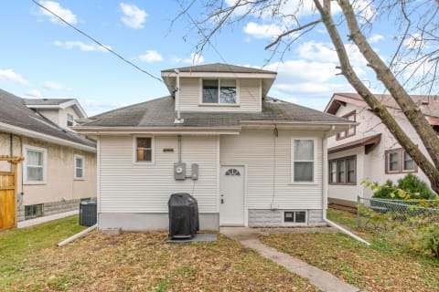Back view of a white two-story house with a peaked roof and a black covered grill.