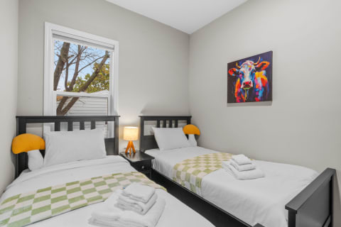 Interior view of a cozy bedroom with two single beds and colorful cow artwork.
