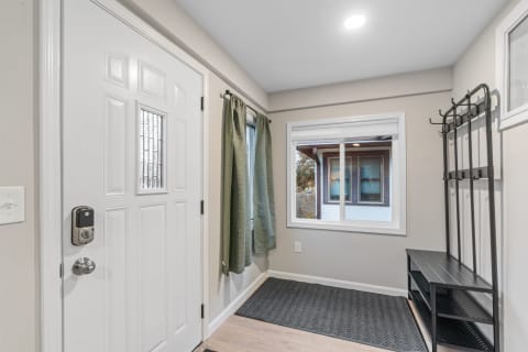 A well-lit entryway featuring a white door, green curtains, and a coat rack.