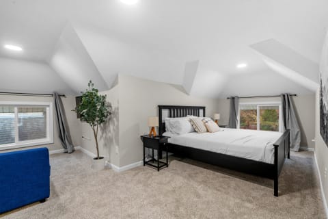 Spacious attic bedroom featuring a black bed, blue sofa, and sloped ceilings.