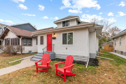 A single-family home with a red door and two red chairs in the front yard.