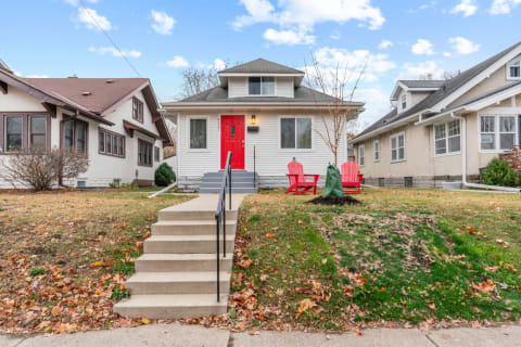 A suburban house featuring a red door, surrounded by colorful fall foliage and red chairs.