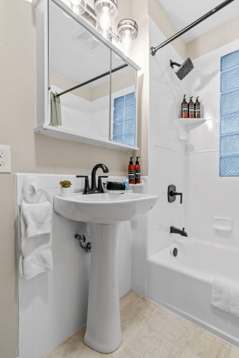 Modern bathroom with white tiles, a pedestal sink, and black fixtures.