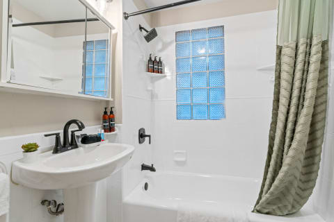 Modern bathroom with a white sink, black faucet, glass brick window, and green shower curtain.