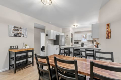 Contemporary kitchen and dining area featuring a black and wood table, white cabinets, and stainless steel appliances.