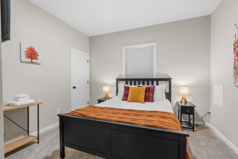 A neatly arranged bedroom with a black bed and colorful throw pillows, soft lighting, and warm decor elements.