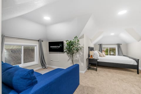 Cozy loft room with blue couch, white bed, and warm carpet.