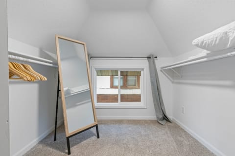 Compact closet with a mirror and wooden hangers, featuring a window with natural light.