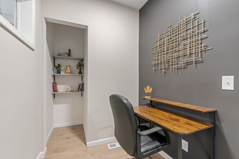 A stylish small office corner with a wooden desk, black chair, and decorative shelves.